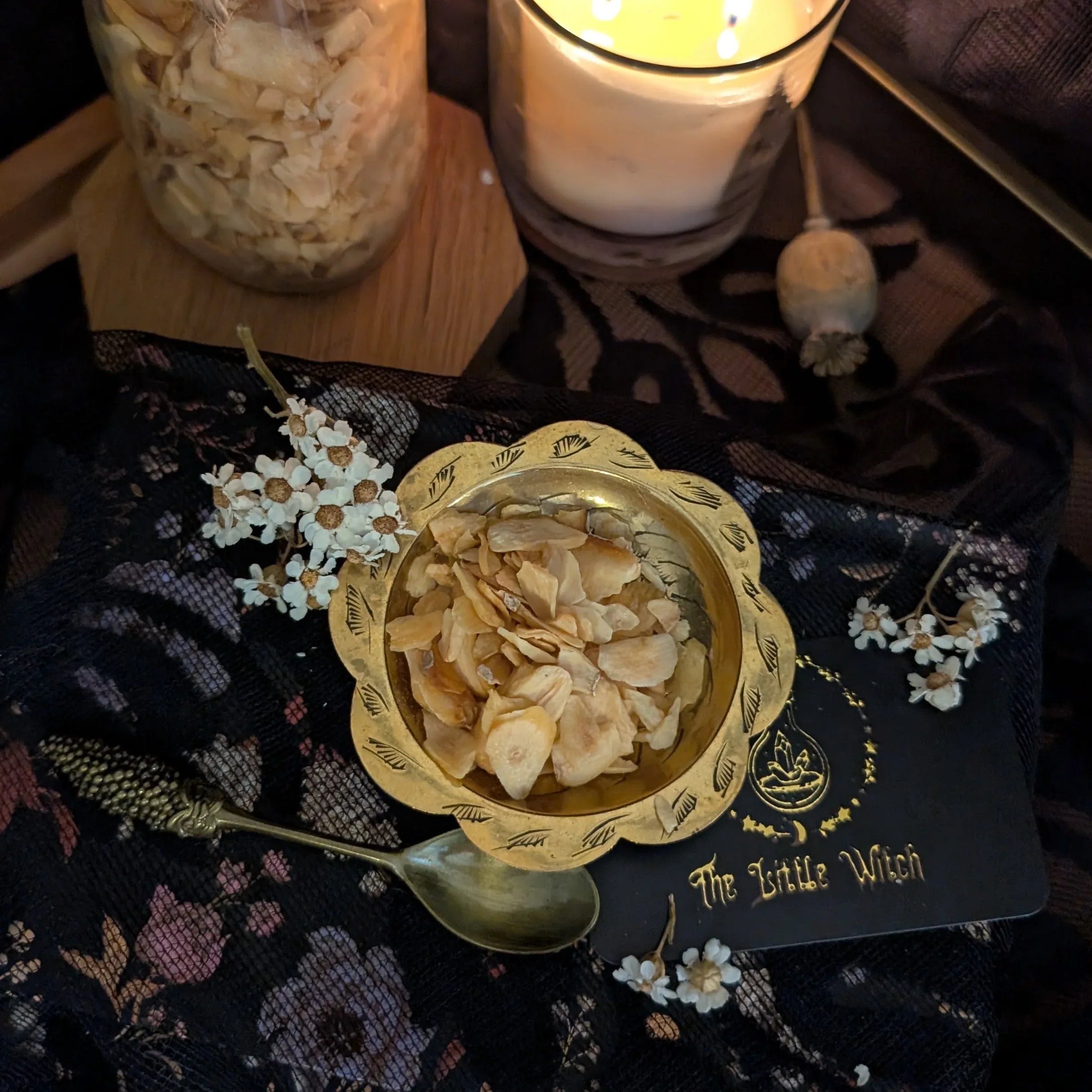 Gold bowl with dried garlic on a dark fabric surface with a candle in the background