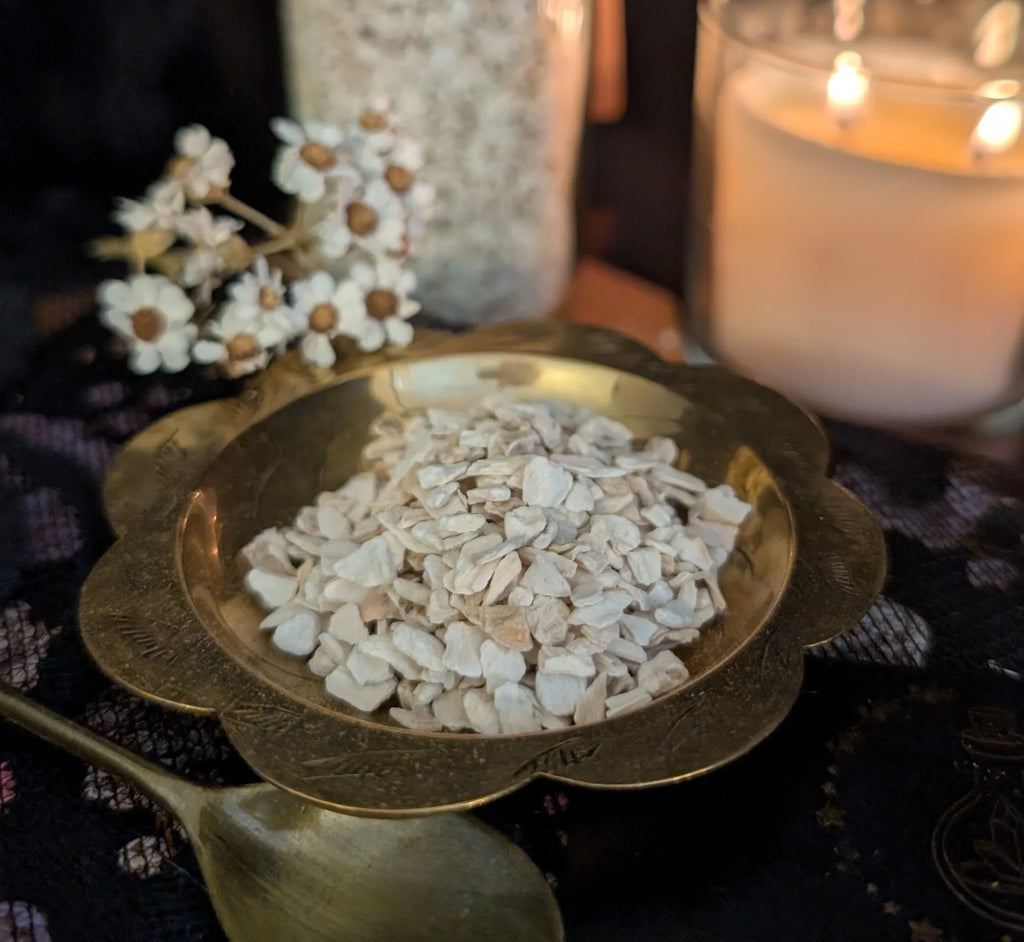 Brass bowl with dried horseradish, spoon, and candle on a dark surface