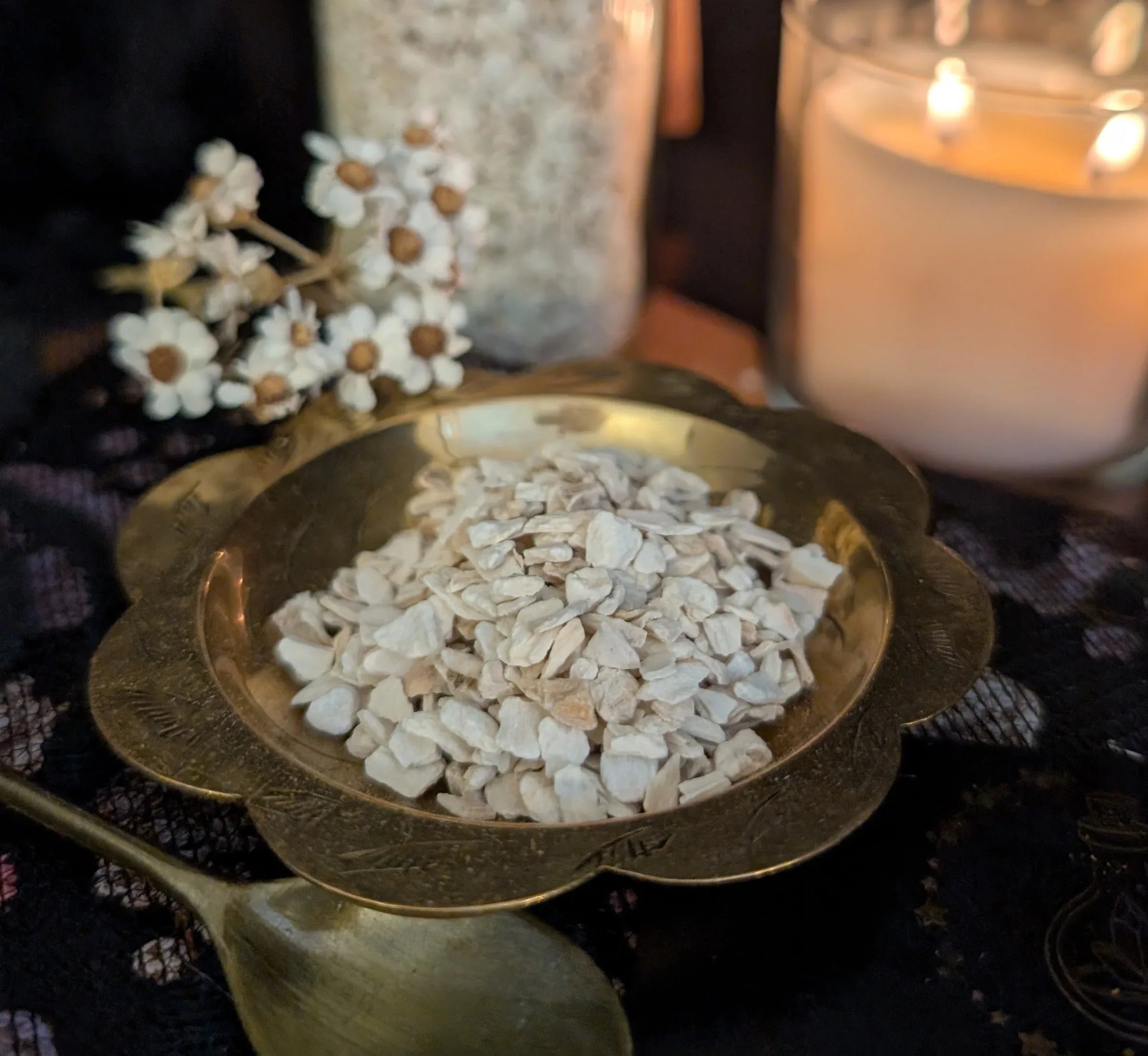Brass bowl with dried horseradish, spoon, and candle on a dark surface