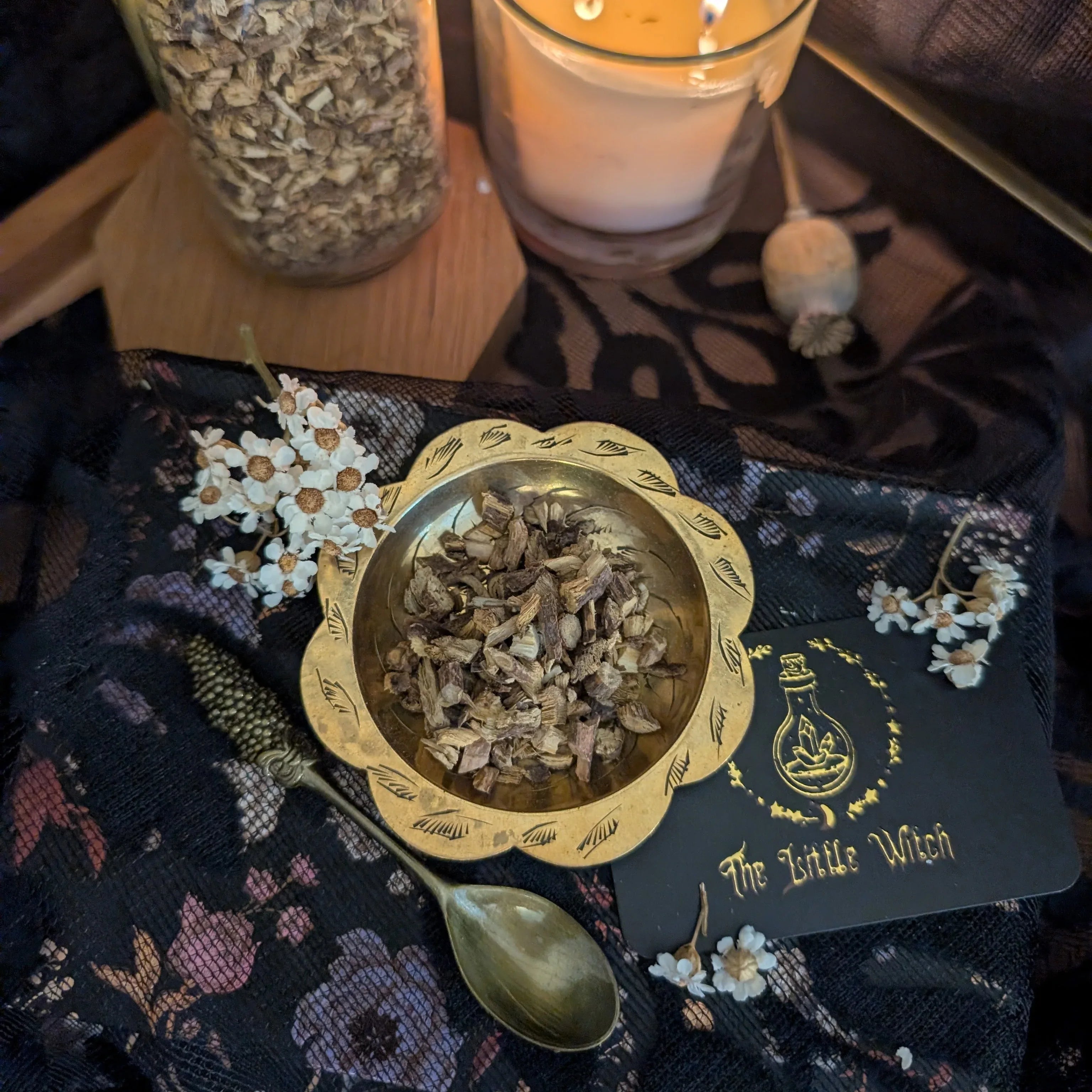 Gold bowl with dried liquorice on a dark fabric background with 'The Little Witch' branding