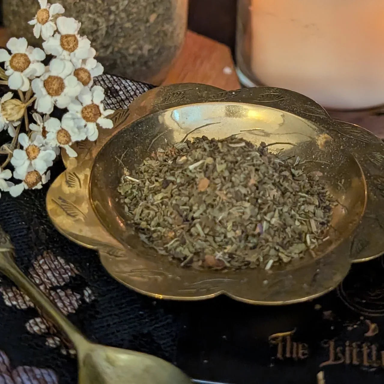 Gold bowl filled with dried  mint herbs on a textured surface with flowers and a candle in the background.