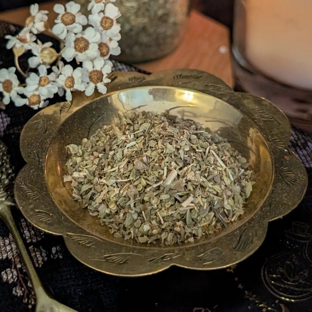dried oregano in a decorative brass bowl with flowers on a dark surface