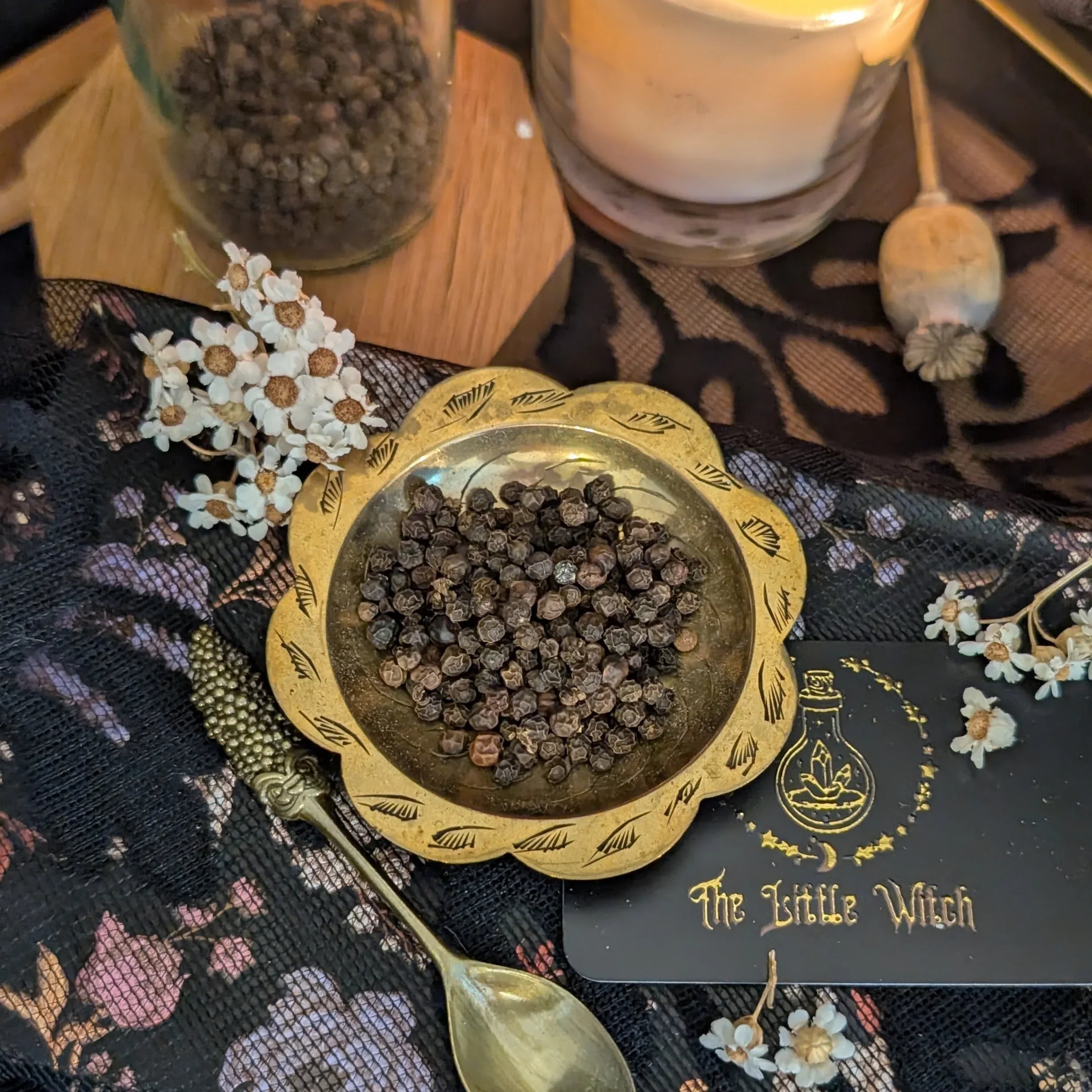 Dried Peppercorns in a dish surrounded by preserved botanicals and a glowing lit candle