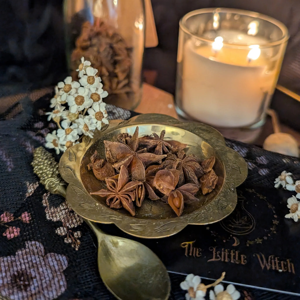 Brass dish with star anise on a dark surface with candles and decorative items.