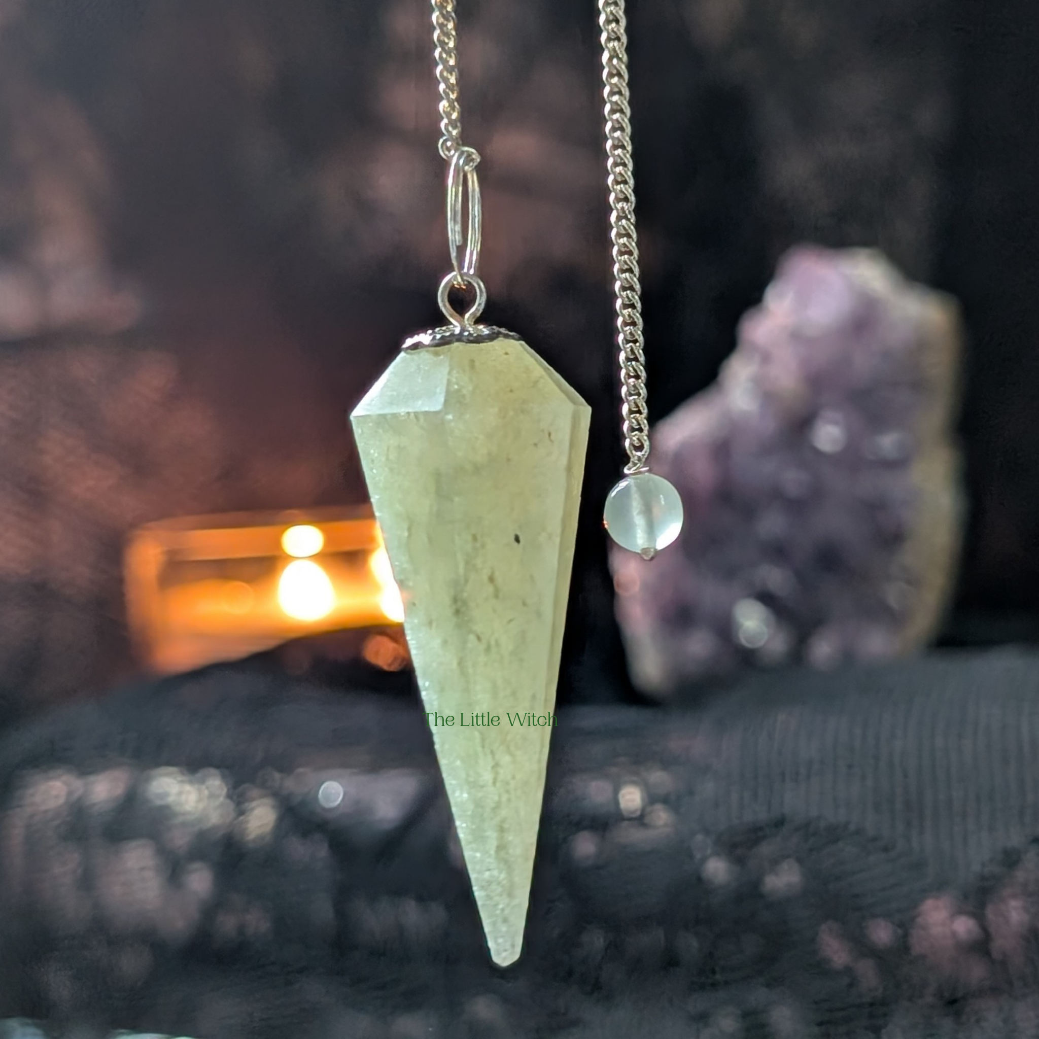 Green Aventurine Pendulum with black lace background. Soft candlelight and a sparkling amethyst geode are in the background 