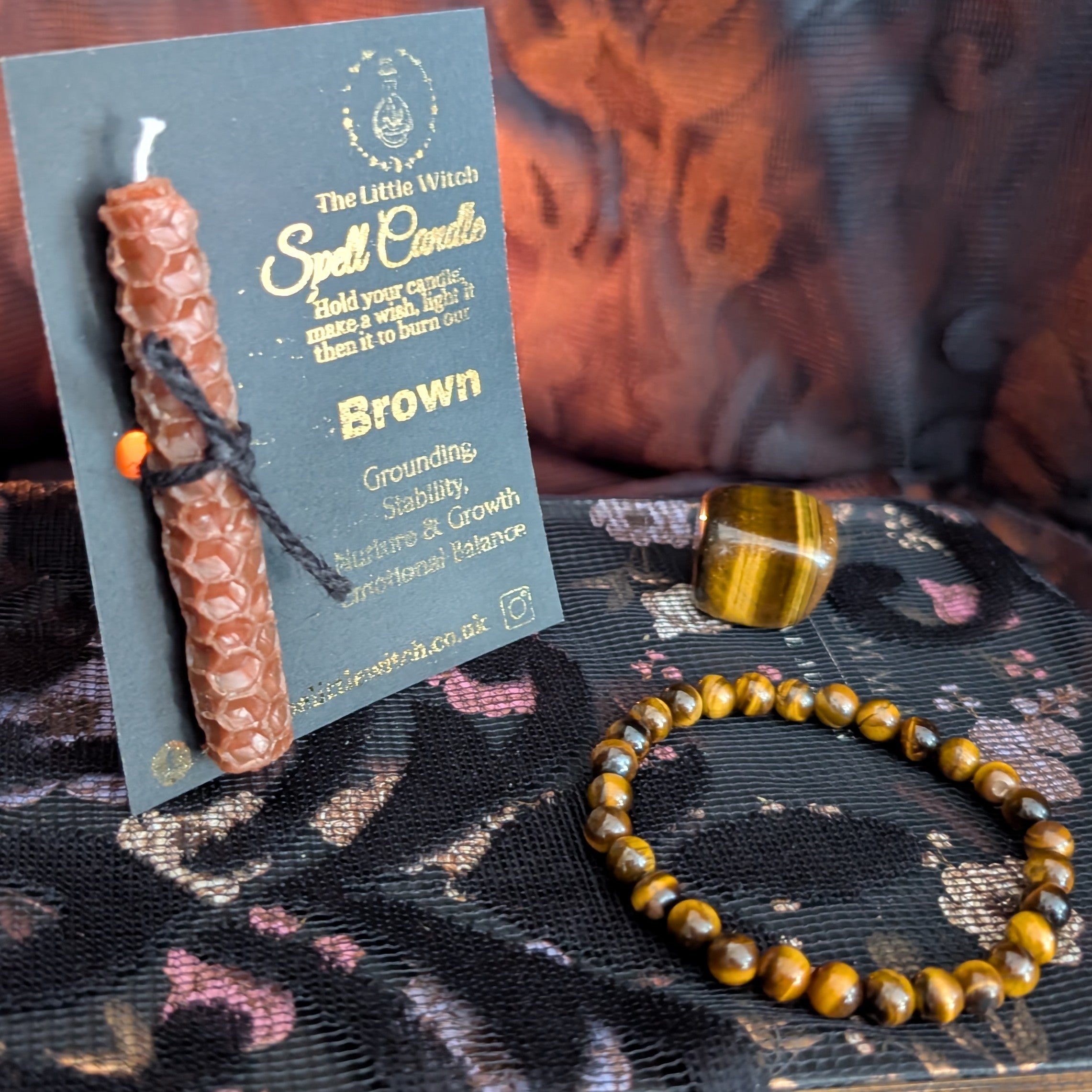 Brown spell candle with packaging and a bracelet on a textured surface