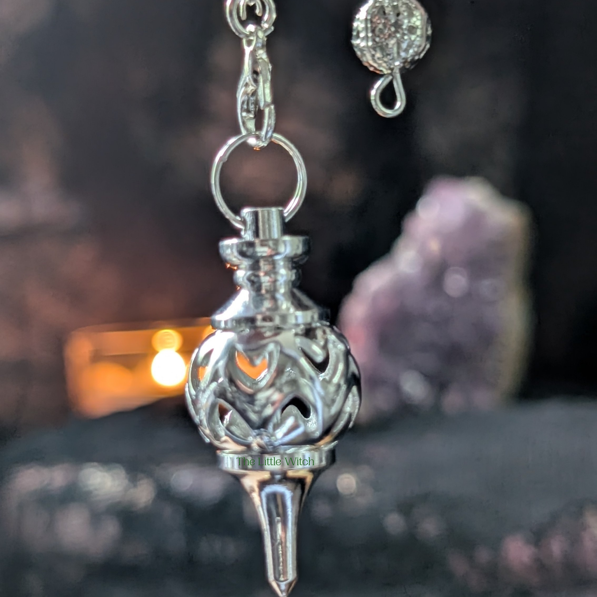 Intricate hearts design in metal pendulum with dark fabric background 