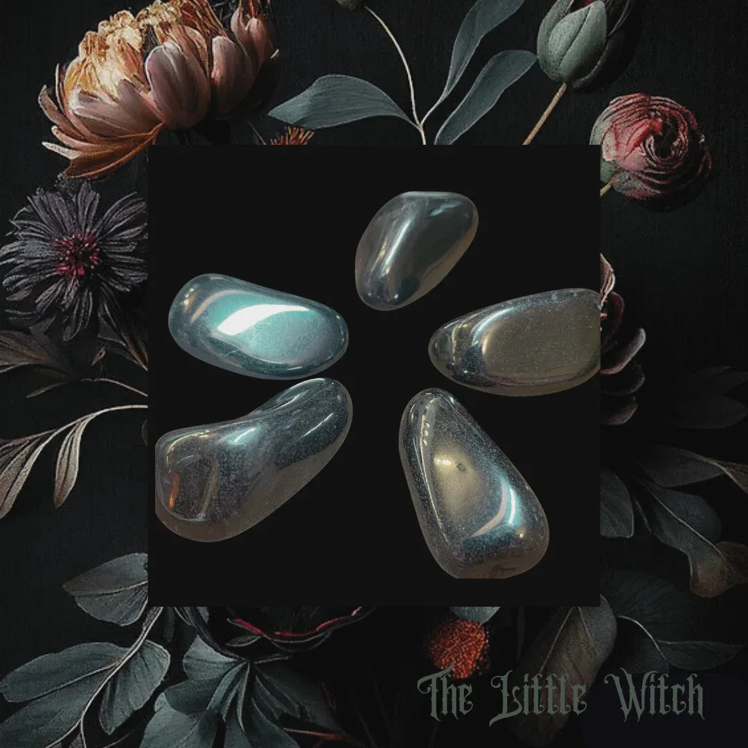 Five smooth stones on a dark surface with floral elements and 'The Little Witch' branding.