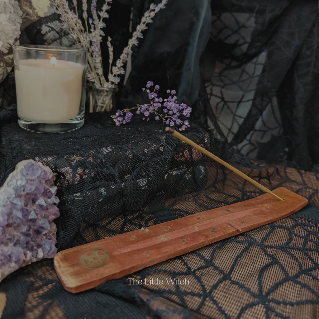 Candle, amethyst crystal, and wooden incense burner on a dark fabric background with 'The Little Witch' branding.