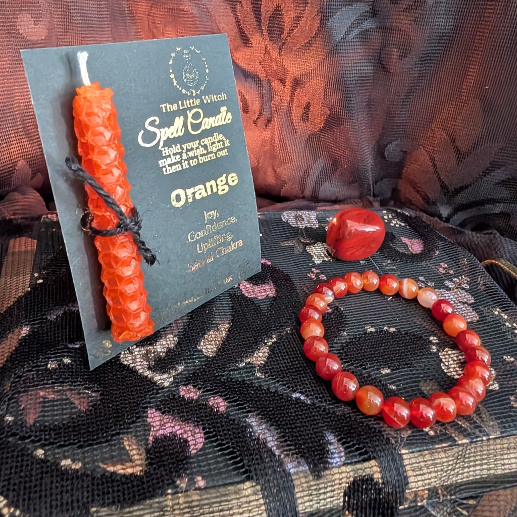 Orange beeswax candle mounted onto The Little Witch branded card with a carnelian agate bracelet and crystal