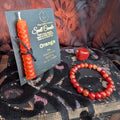 Orange beeswax candle mounted onto The Little Witch branded card with a carnelian agate bracelet and crystal