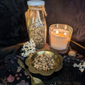 dried liquorice in a bowl with a lit candle and bottle on a dark surface.