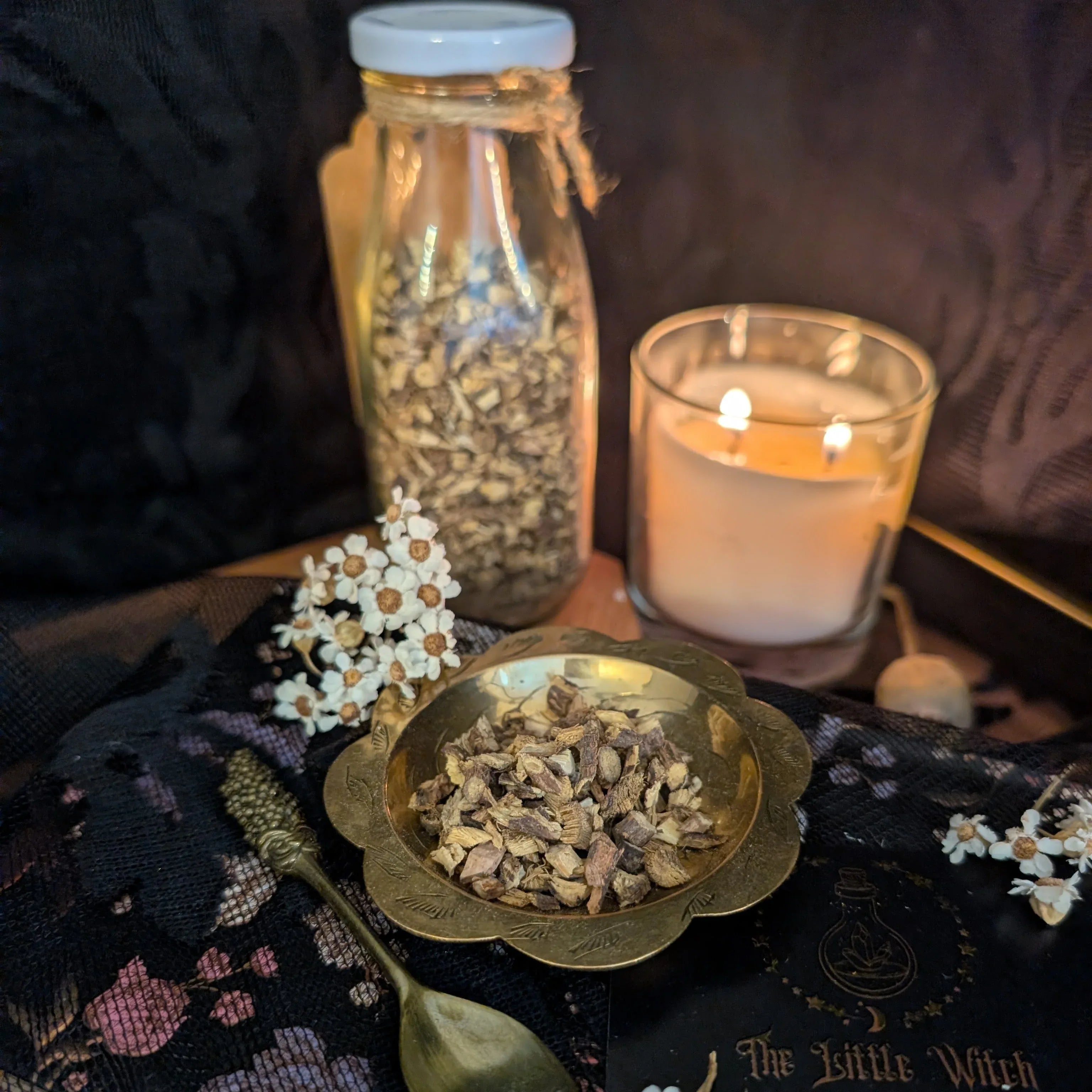 dried liquorice in a bowl with a lit candle and bottle on a dark surface.