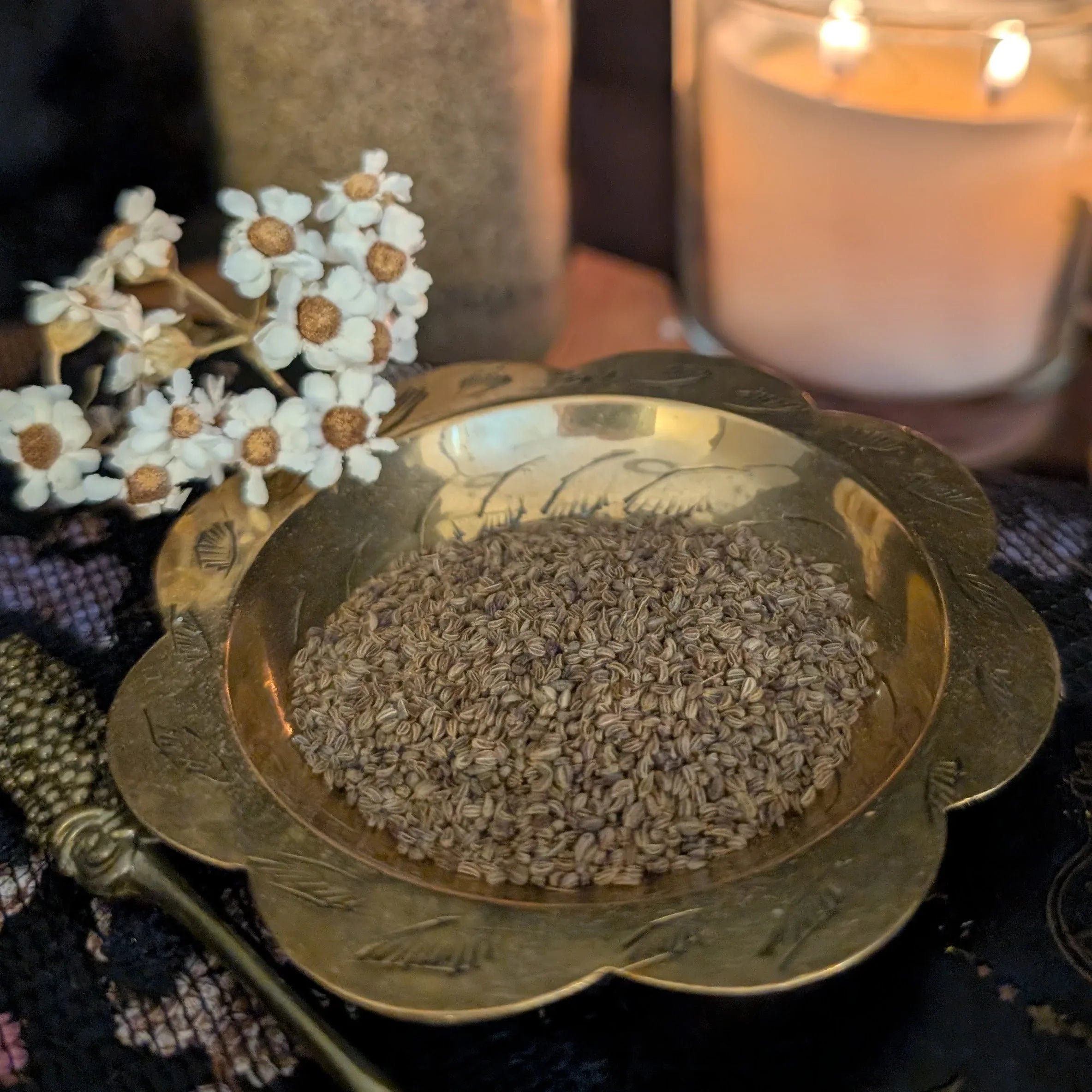 Brass dish with lovage seeds, white flowers, and a candle in the background