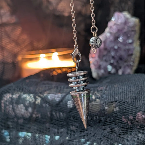 metal pendulum on a chain against a mystical background with crystals and fire.