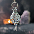 Metal ball pendulum with heart design on a dark background with candlelight and amethyst geode 