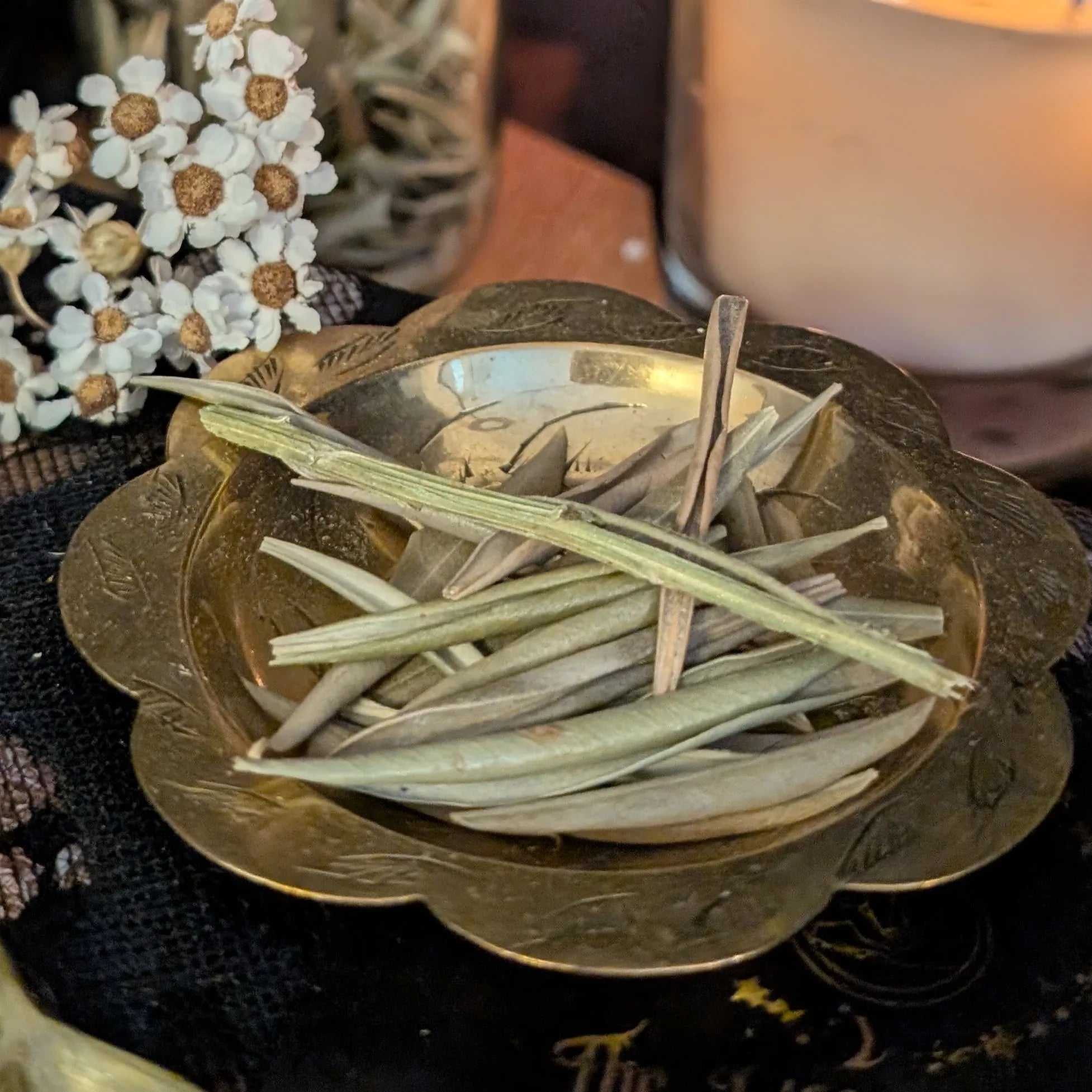 Dried Olive leaves in a decorative brass bowl with flowers in the background