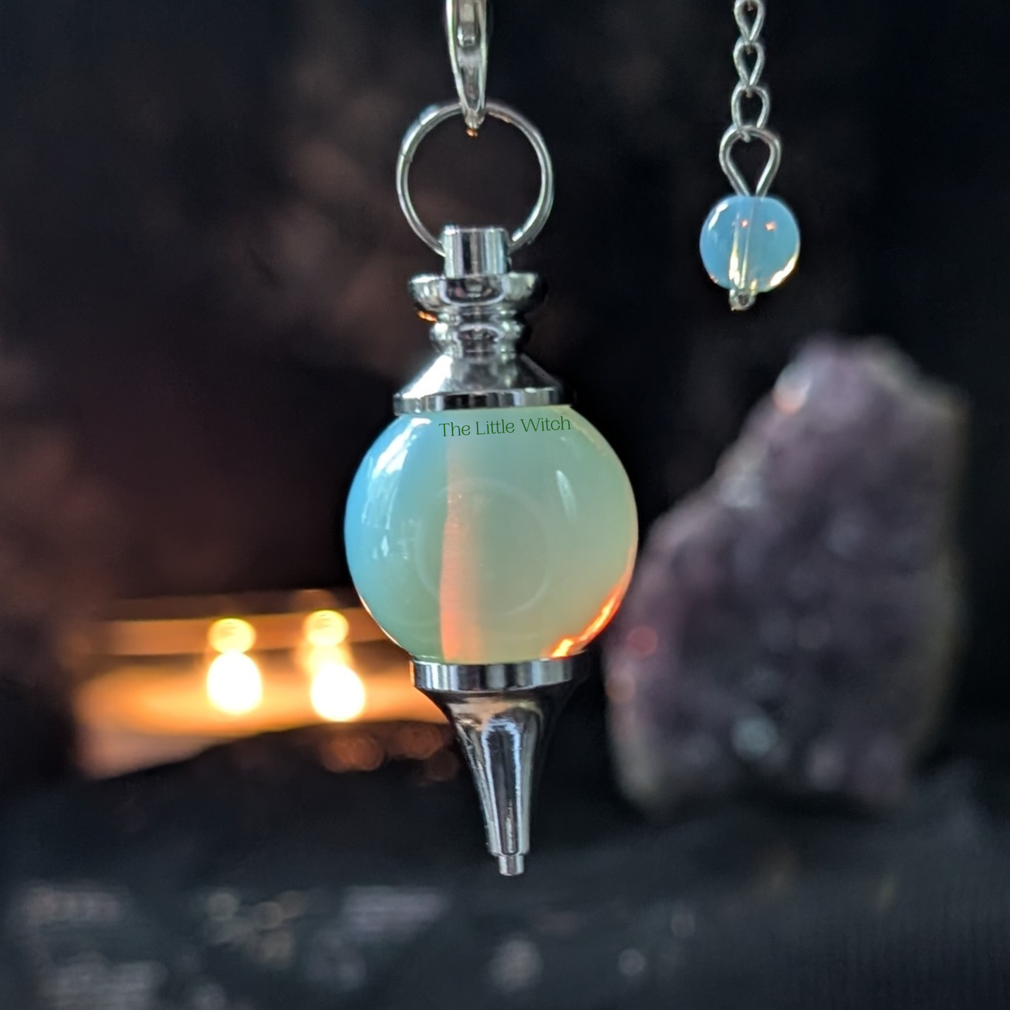 Decorative pendulum with a glowing orb and metallic top, set against a dark background.