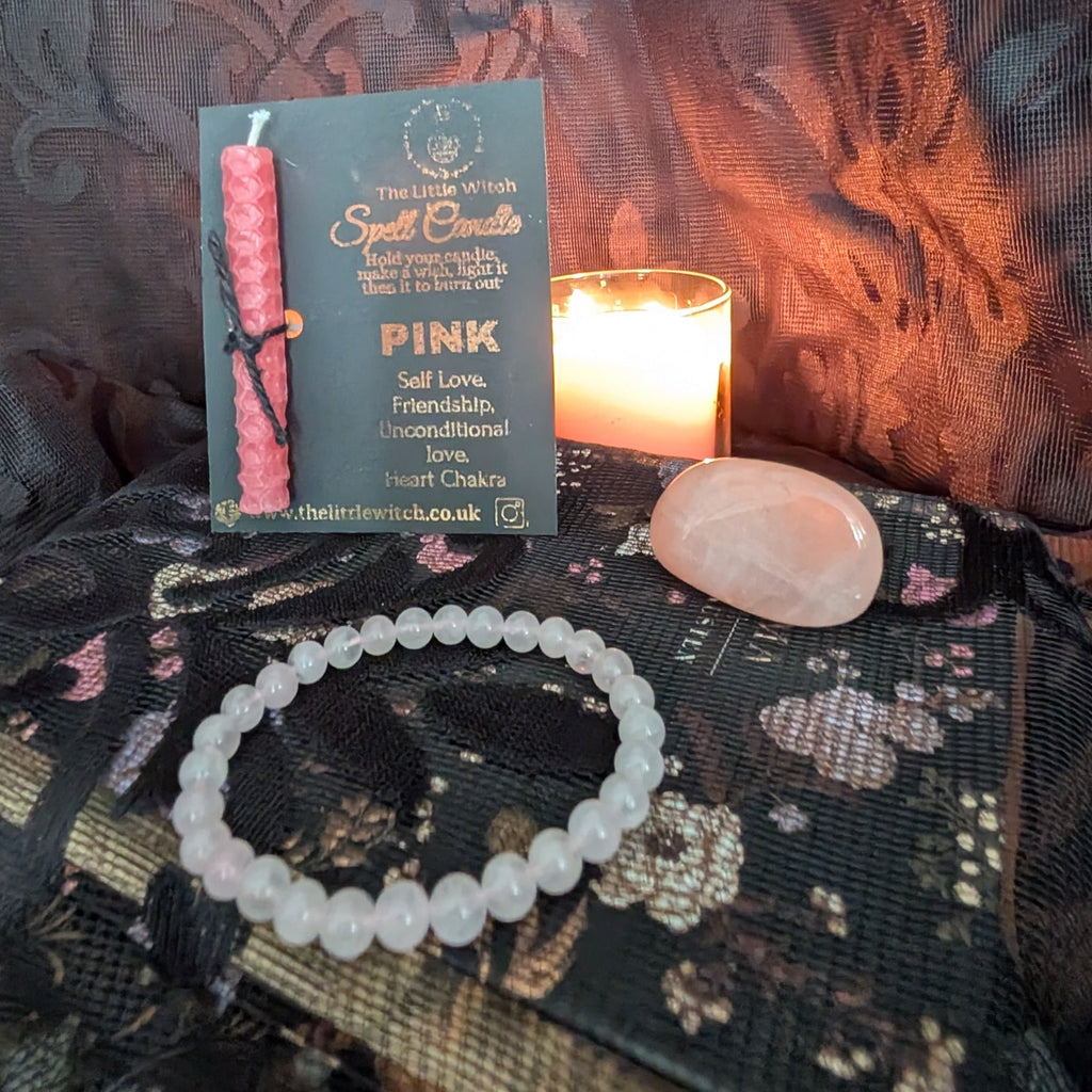 Pink candle, bracelet, and crystal on a textured surface with a lit candle in the background.