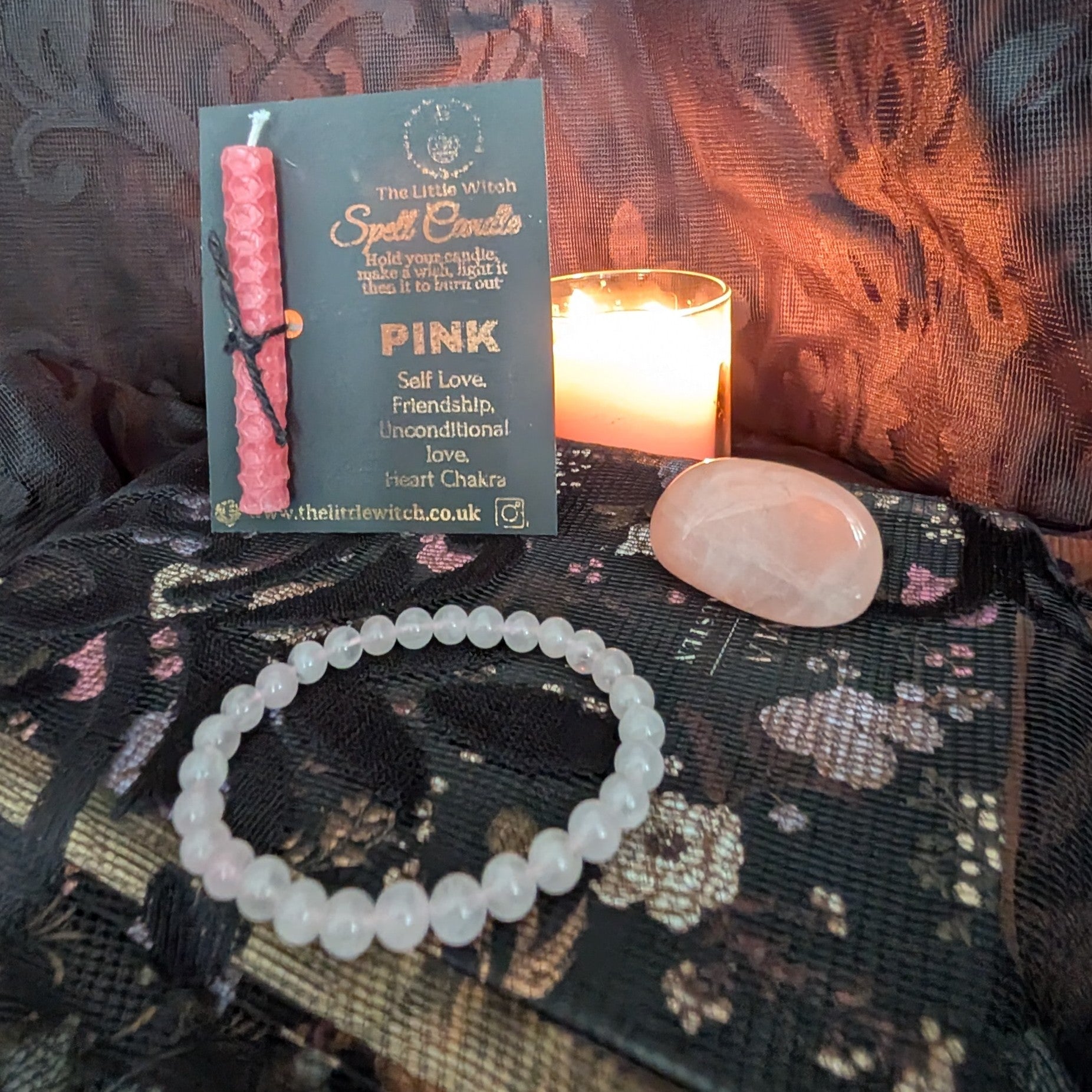 Pink candle, bracelet, and crystal on a textured surface with a lit candle in the background.