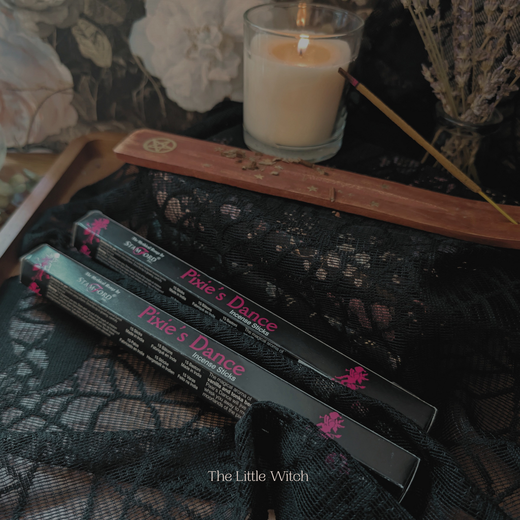 Two boxes labeled 'Pixie's Dance' by 'The Little Witch' on a dark fabric background with a lit candle.