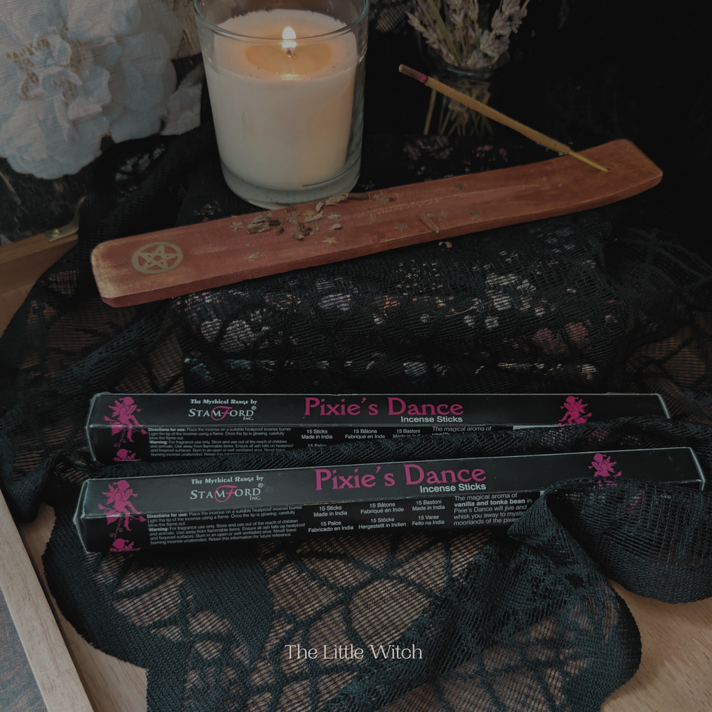 Pixie's Dance incense sticks with packaging on a dark surface next to a lit candle.