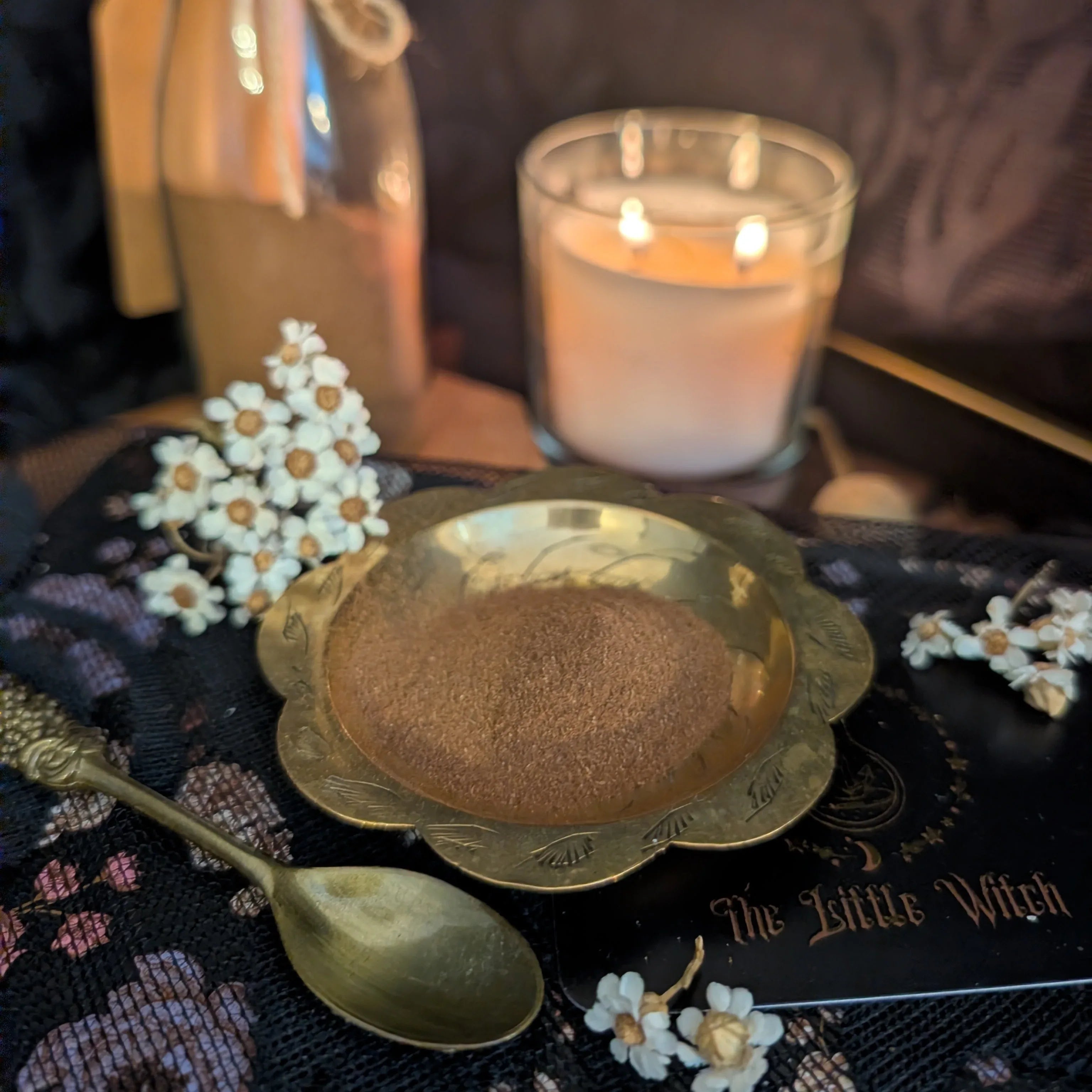 Candle, spoon, and decorative items on a dark surface with 'The Little Witch' branding.