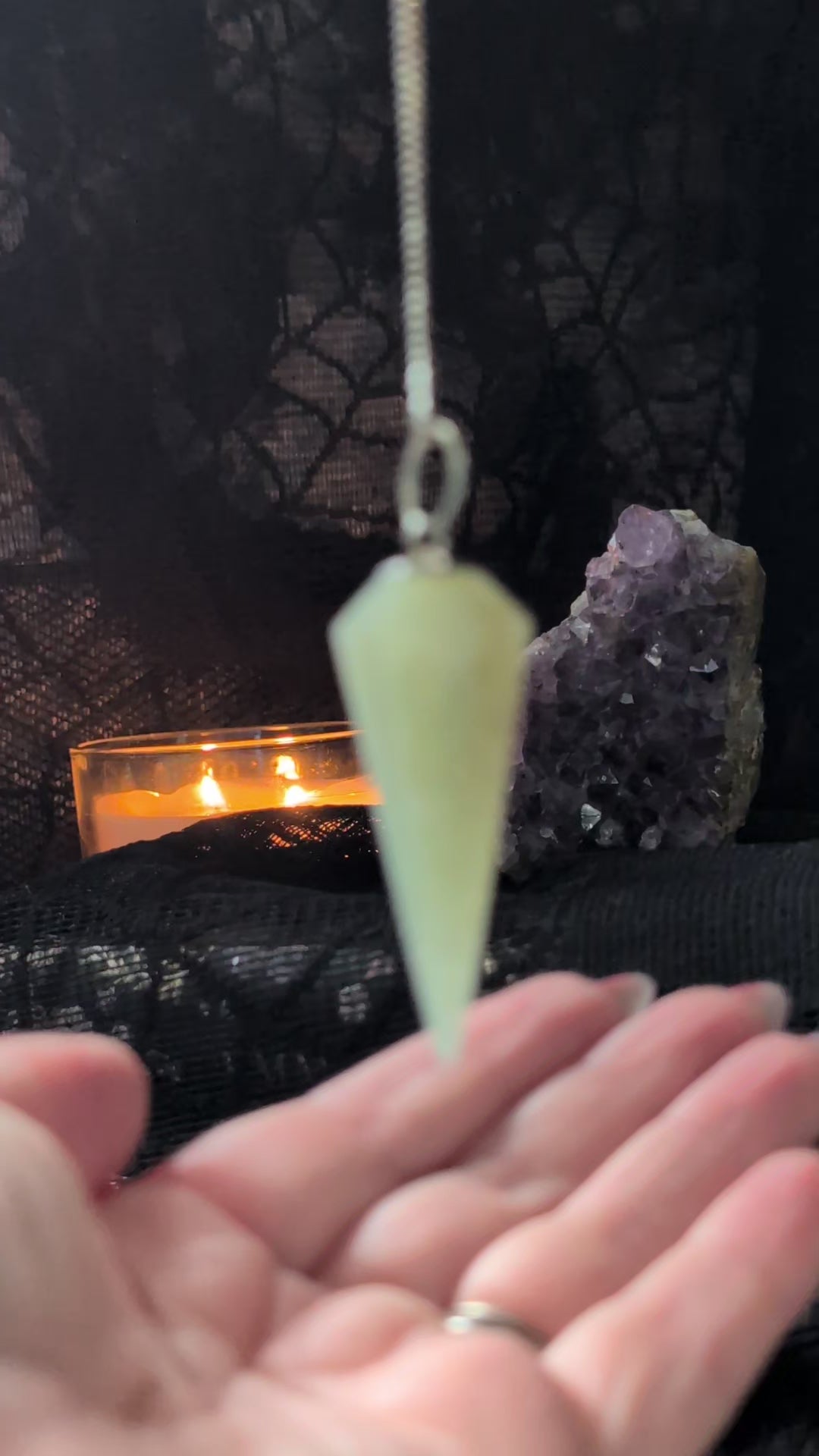 Green Aventurine Pendulum answering yes or no questions with black lace background, an amethyst geode and lit candle are also in the background 