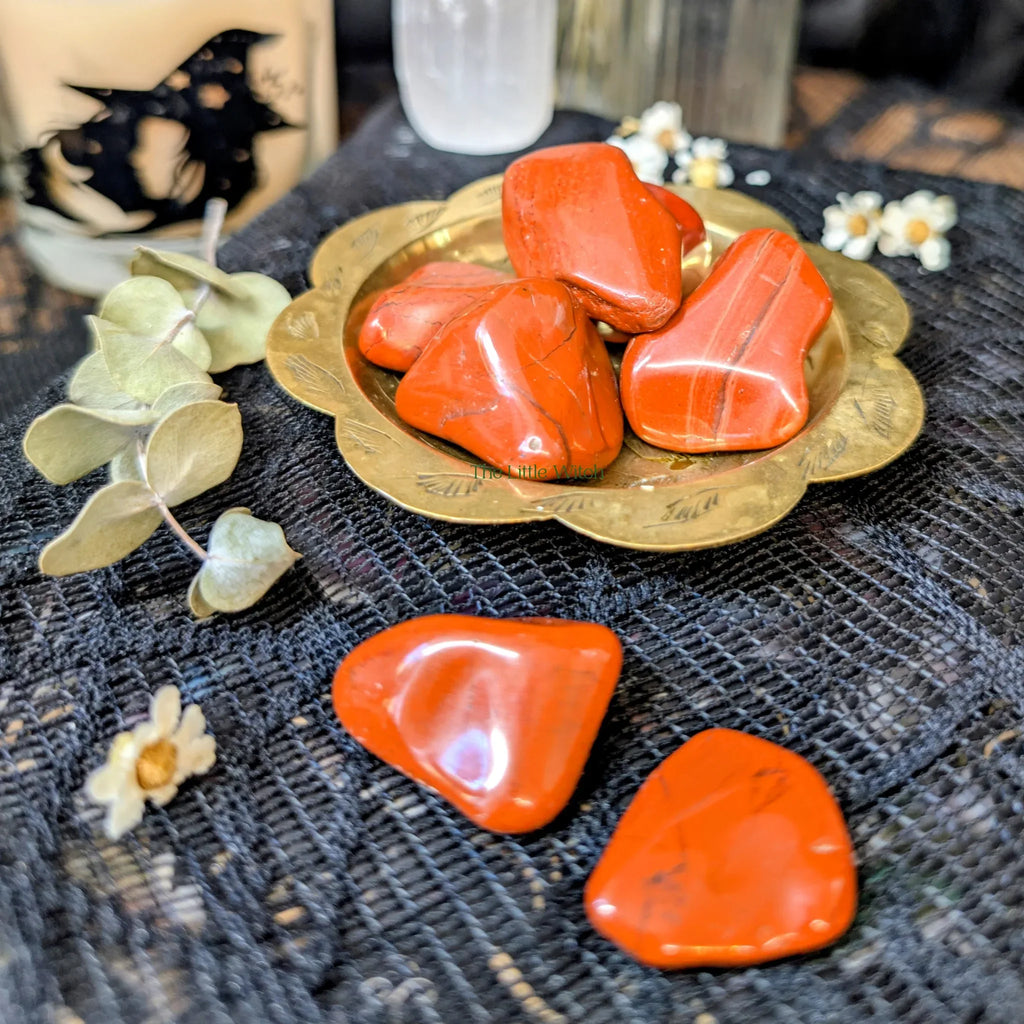 Red jasper crystals on a brass tray with eucalyptus leaves and flowers on a textured surface