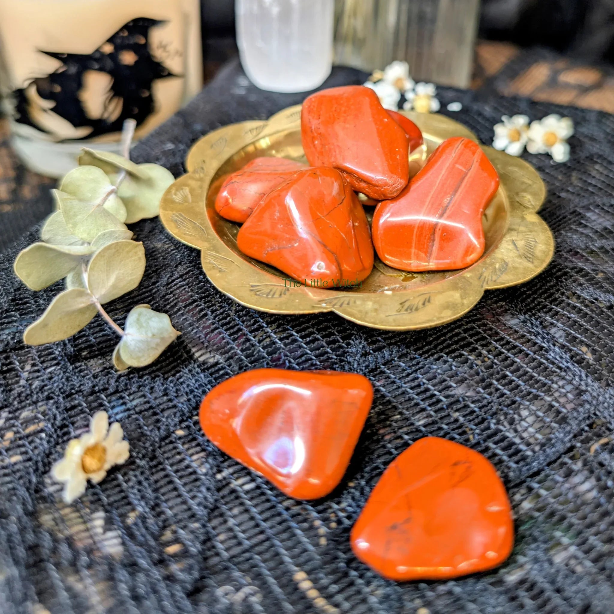 Red jasper crystals on a brass tray with eucalyptus leaves and flowers on a textured surface