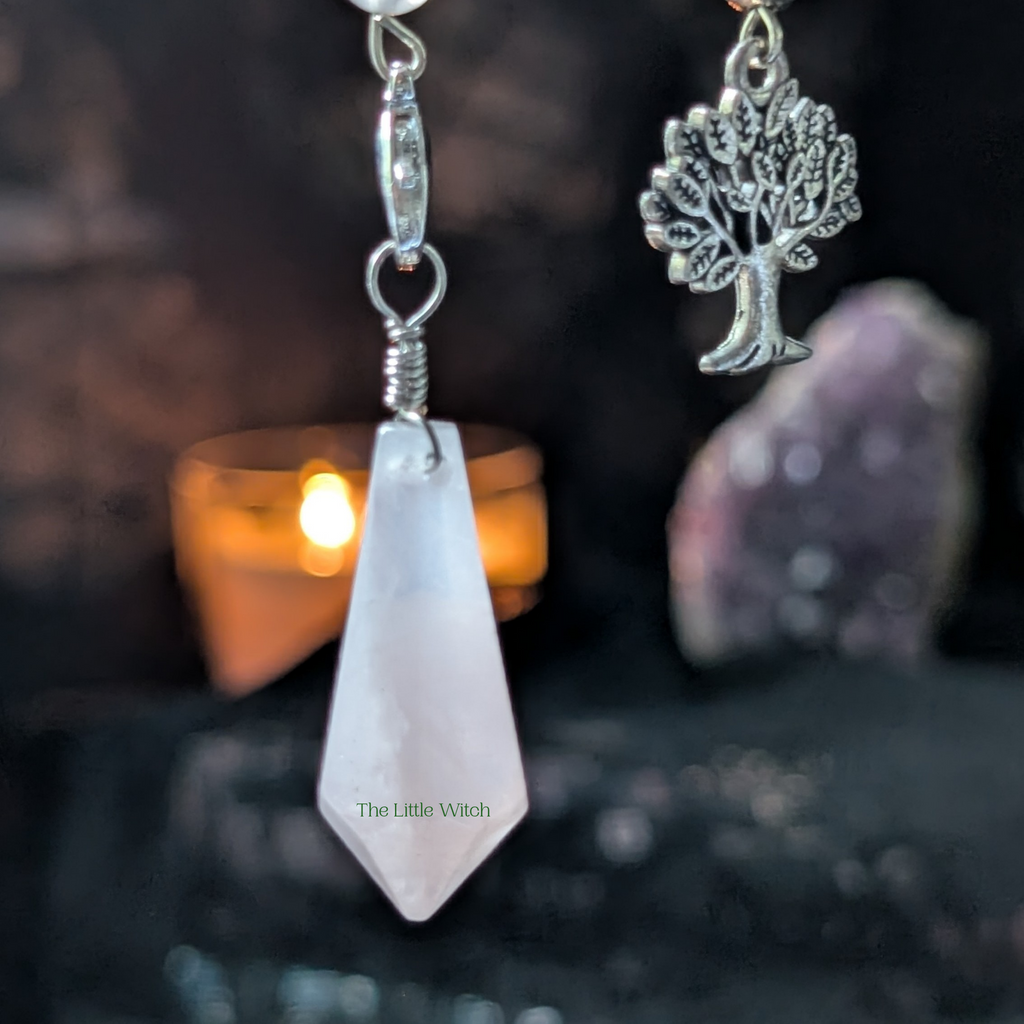 Rose Quartz pendulum with a tree-shaped pendant on a dark background.