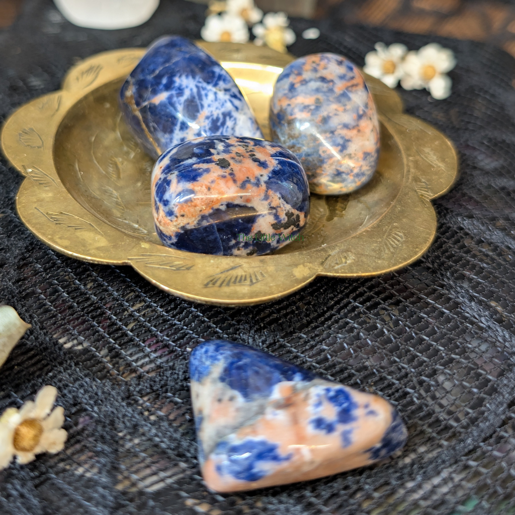 Three blue and pink stones on a decorative gold plate with flowers in the background