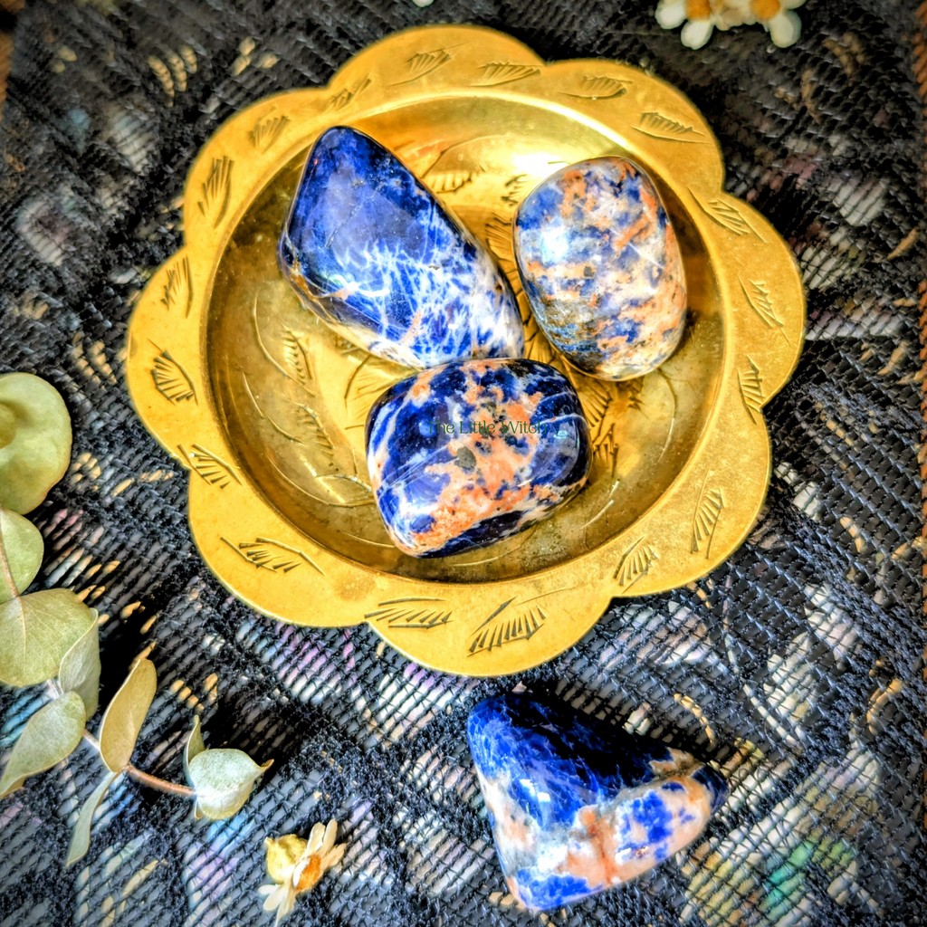 Three blue and orange stones on a gold dish with a textured black background