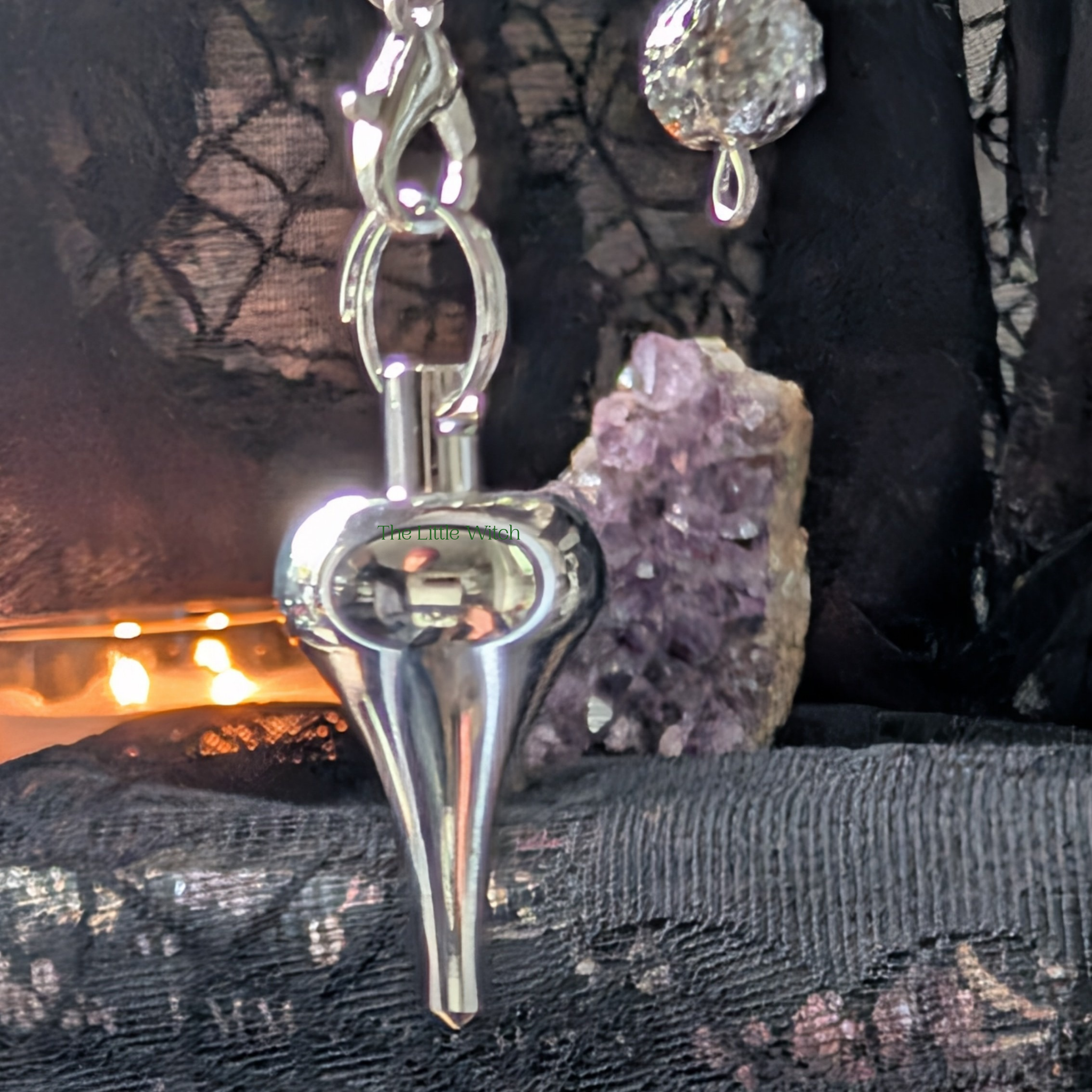 Teardrop shaped pendulum with a black cloth background, a softly lit candle and an amethyst geode 