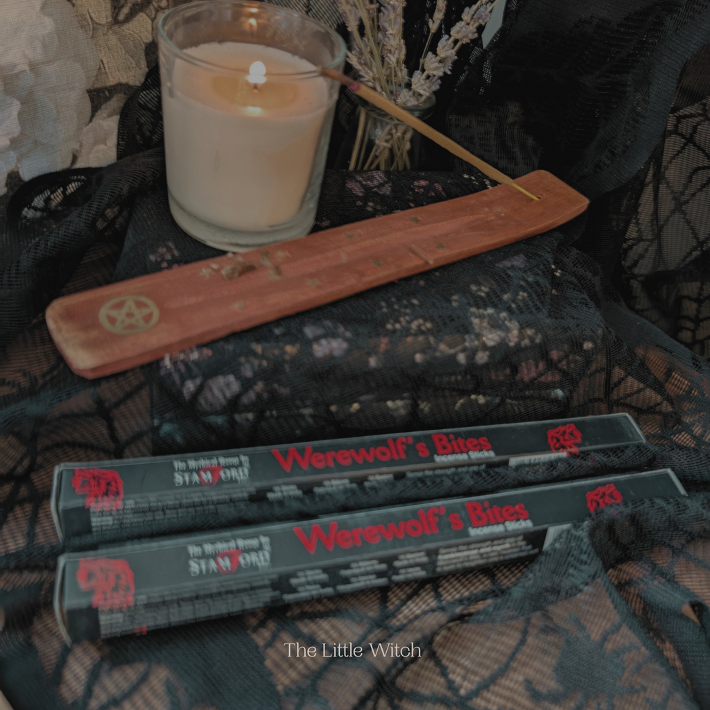 Candle with a pentacle holder and 'Werewolf's Bites' incense boxes on a textured surface.