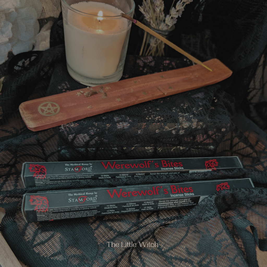 Werewolf's Bites incense sticks with a lit candle and wooden holder on a dark fabric background.